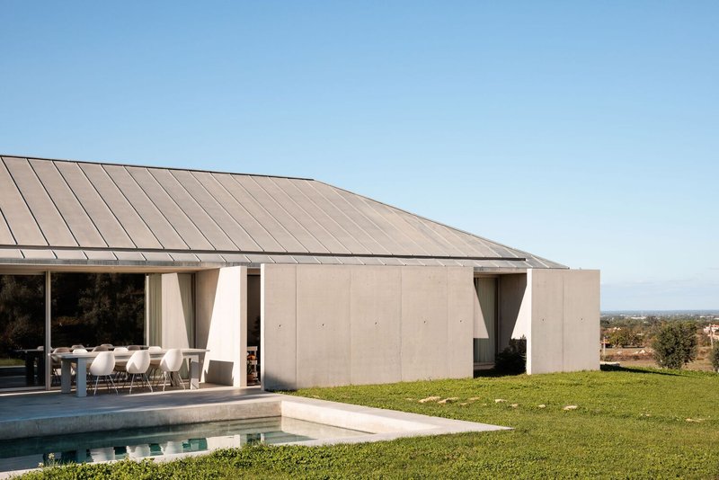 Covered terrace with tapered concrete columns beside a pool and lawn under clear sky