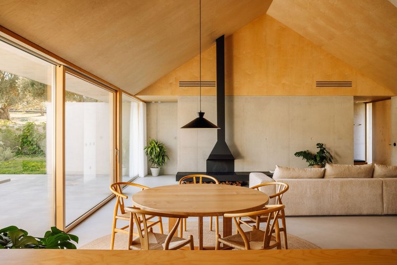 Dining area with plywood vaulted ceiling and suspended fireplace opening to garden through timber-framed glazing