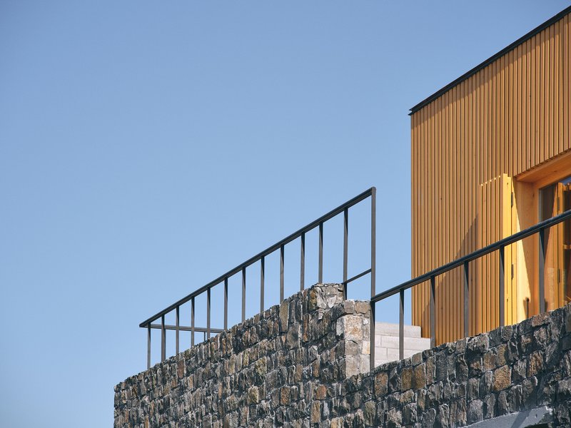 Detail of the steel railing atop a dark stone wall with vertical timber cladding beyond