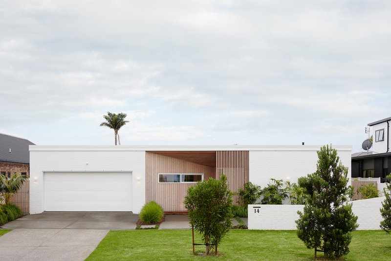 Street view of white brick facade with vertical timber cladding and front lawn with palm tree