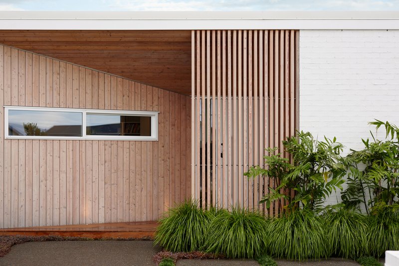 Timber-clad facade with vertical slat screen and horizontal ribbon window beside planted garden bed