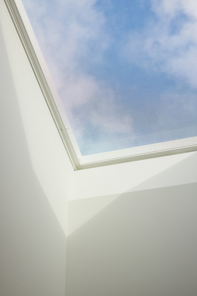 Rectangular skylight framed in white plaster walls beneath a blue sky with scattered clouds