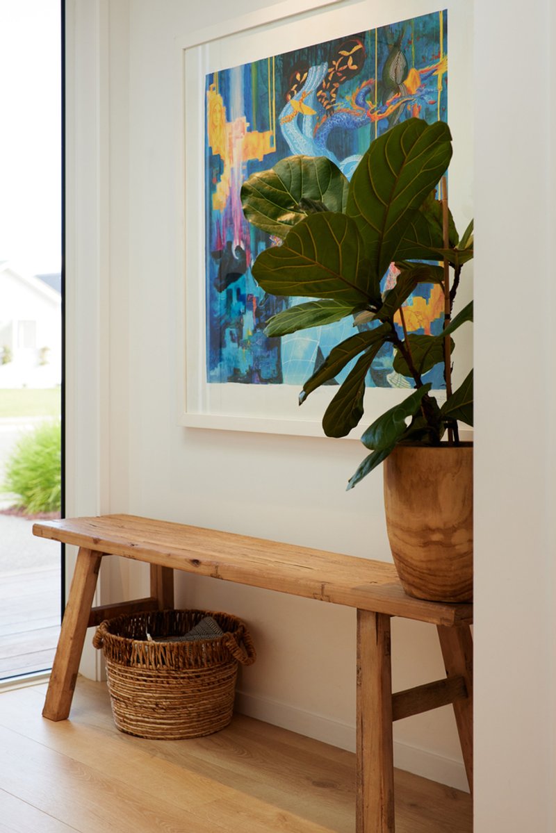 Timber bench with fiddle-leaf fig in terracotta pot and woven basket below a framed artwork