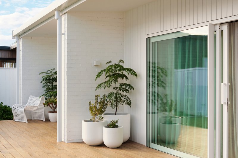 Covered timber deck with white painted brick wall, sliding glass door, and potted plants in planters