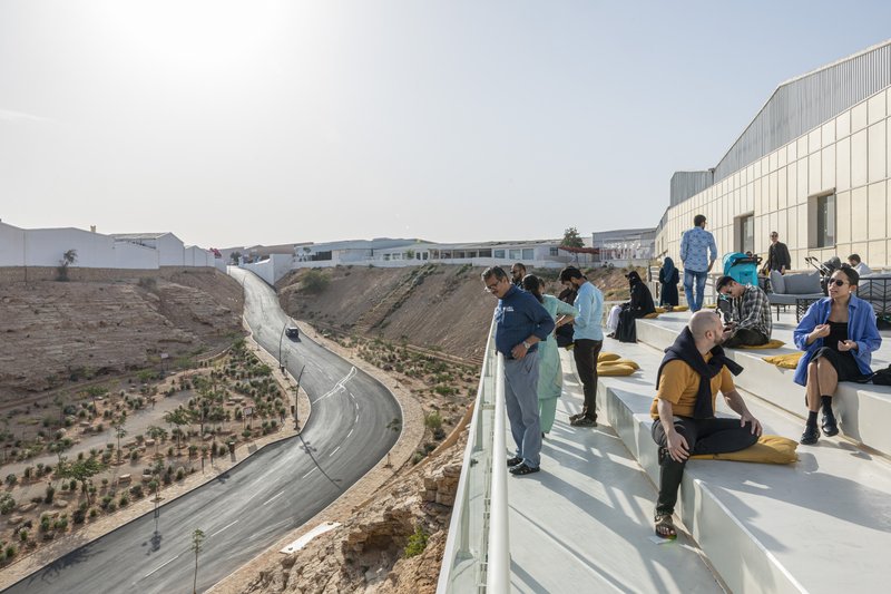 Rooftop terrace overlooking a curving drainage canal with planted embankments and seated visitors