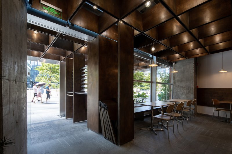 Interior dining area with coffered timber ceiling, steel columns, and glazed storefront opening to pedestrians outside
