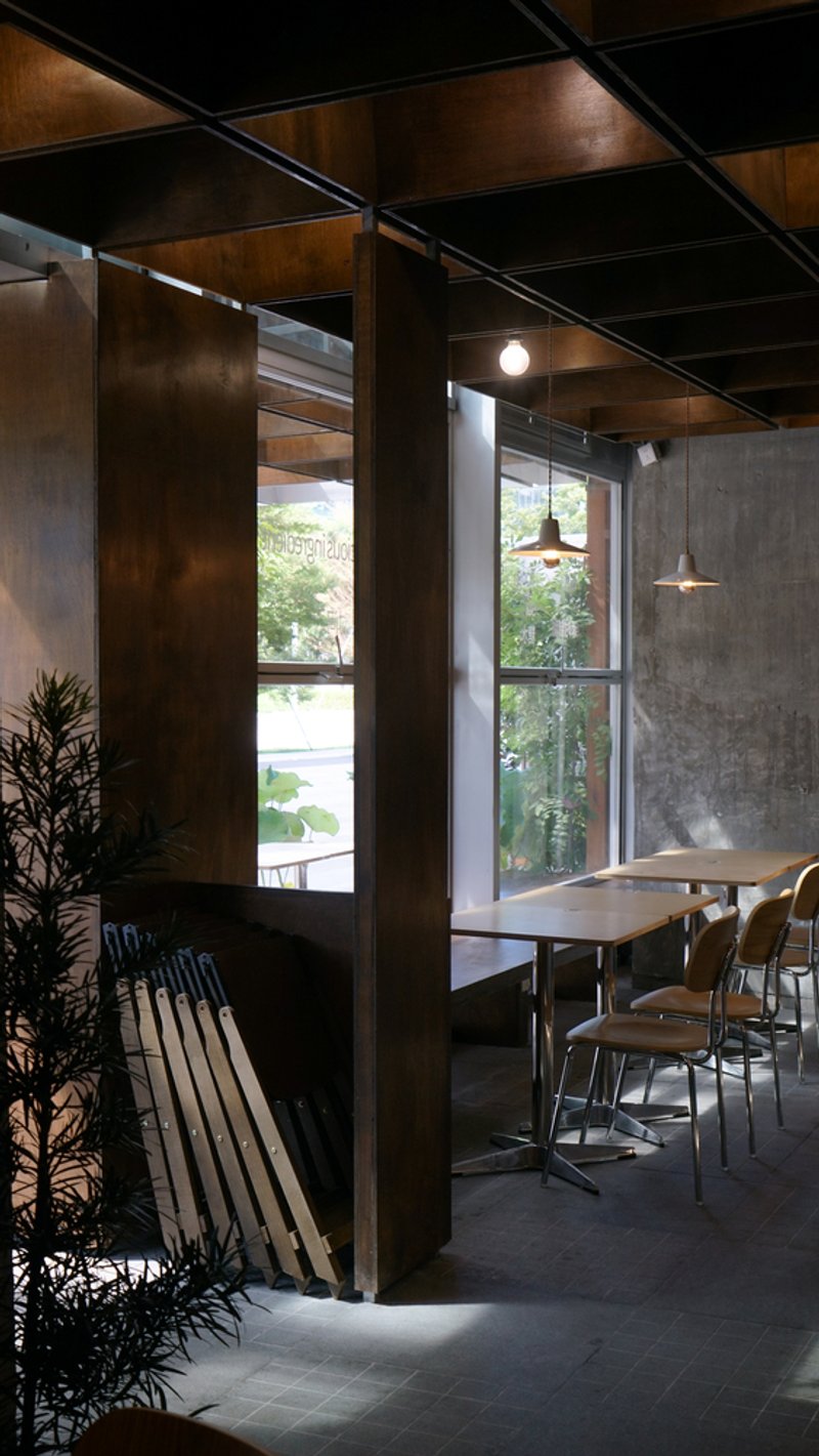 Corner seating nook with dark timber columns, potted plant, and pendant lights beside street-facing windows