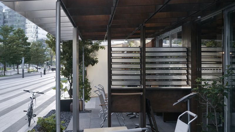 View through the open pavilion showing horizontal slatted screens and steel structural frame with pedestrians beyond