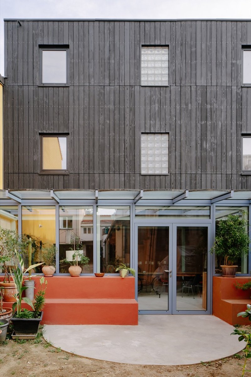 Charred wood facade with glazed ground floor extension and coral-painted planters at twilight