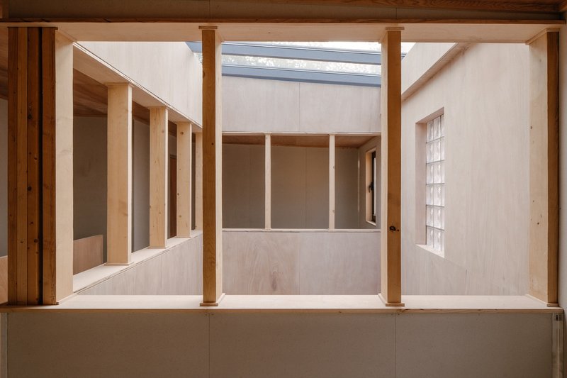 Double-height interior courtyard with plywood walls, timber columns and a linear skylight above