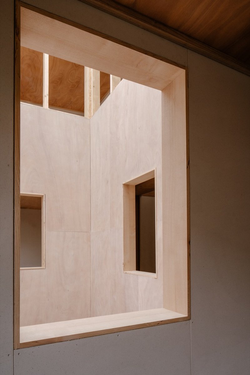 View into a plywood-lined room with clerestory windows and integrated shelving under a timber ceiling