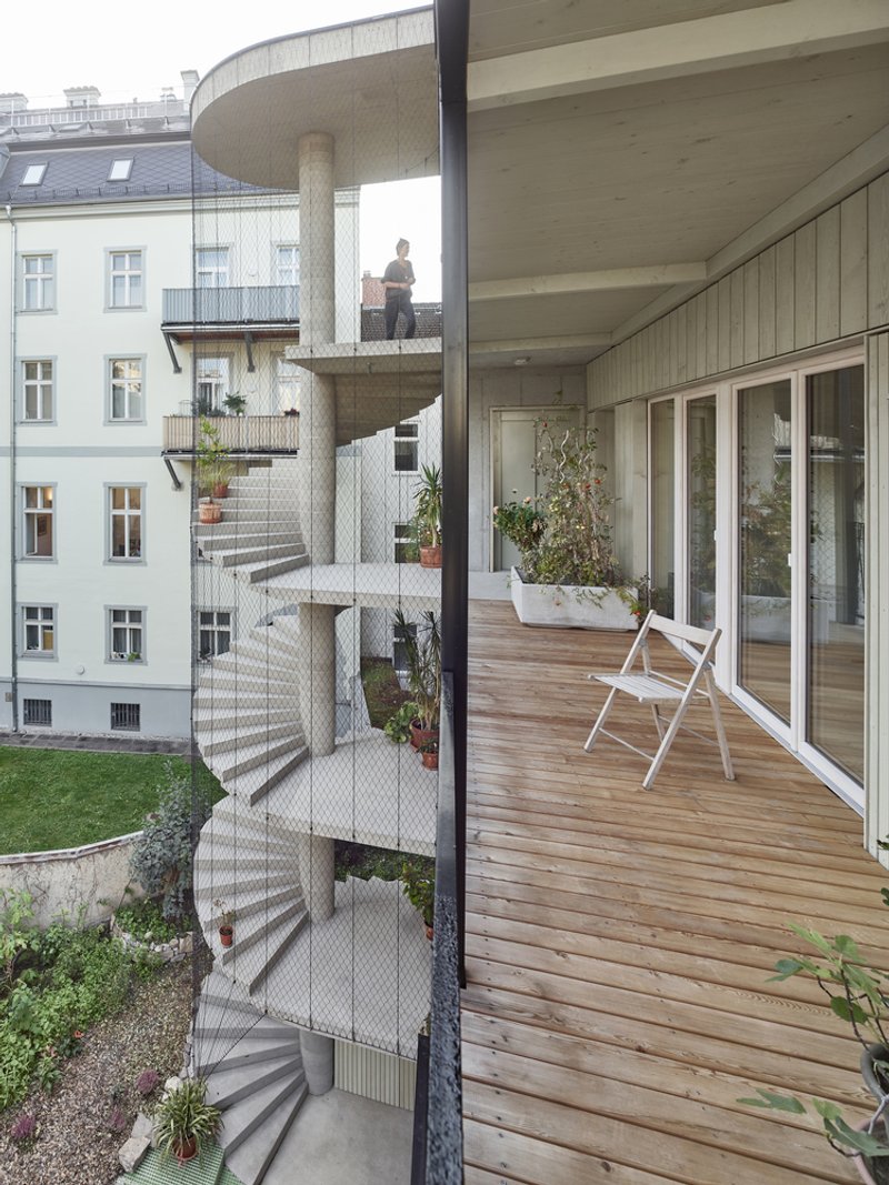 Timber balcony deck with white folding chair looking out toward the spiraling concrete stair tower clad in mesh