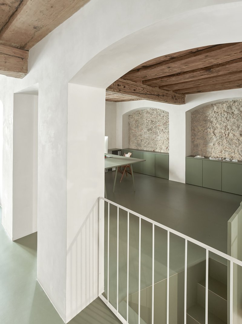 Split-level interior with exposed timber beams and olive-green cabinetry beneath textured stone arches