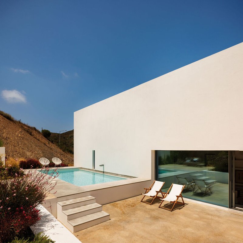 White stucco volume with swimming pool and stepped terrace against a hillside under clear blue sky
