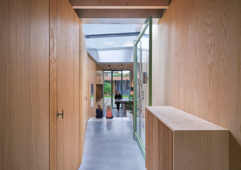 Wood-lined corridor with skylight and pale green door leading to garden courtyard with occupants
