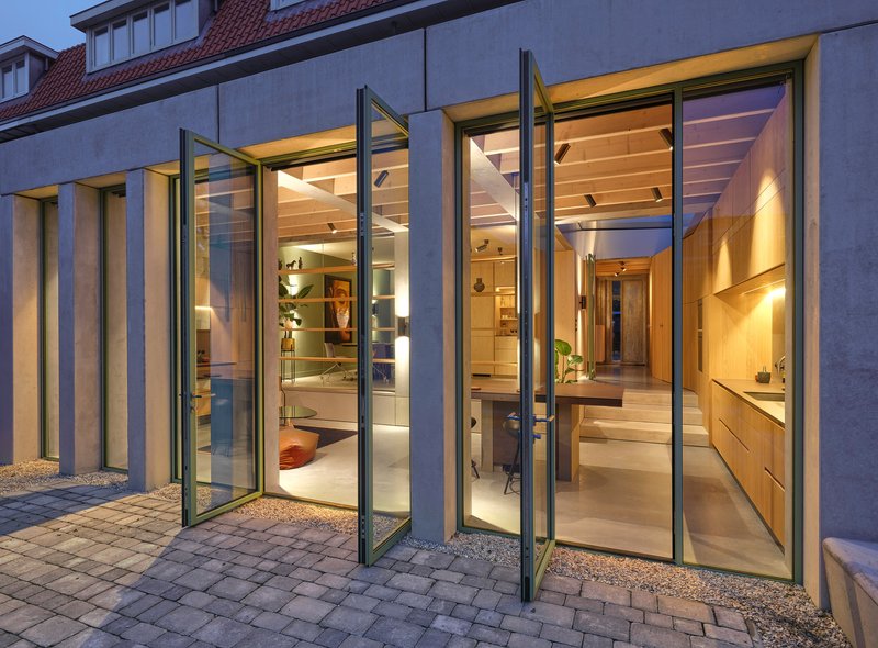 Folding glass doors opening from a paved courtyard into the illuminated interior at dusk