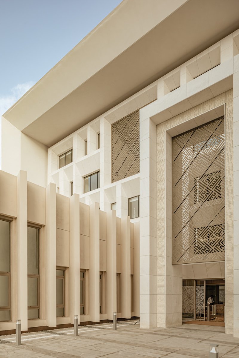Covered entrance courtyard with vertical stone fins and patterned geometric screen panel under clear skies
