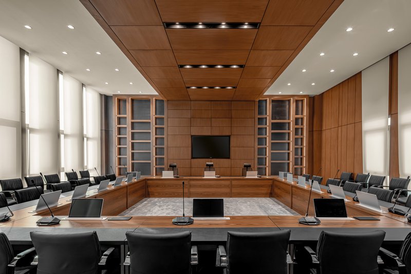Timber-paneled council chamber with U-shaped seating arrangement and integrated ceiling downlights