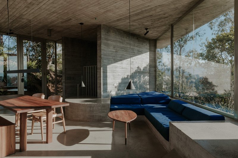Living space with board-formed concrete walls, timber ceiling, and blue upholstered built-in seating catching afternoon sun