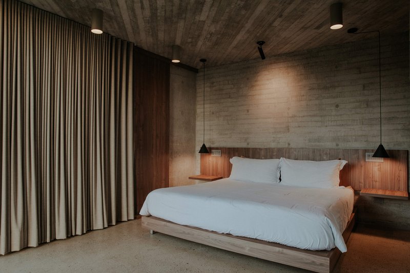 Bedroom with walnut headboard and nightstands beneath board-formed concrete walls and ceiling with pendant lights