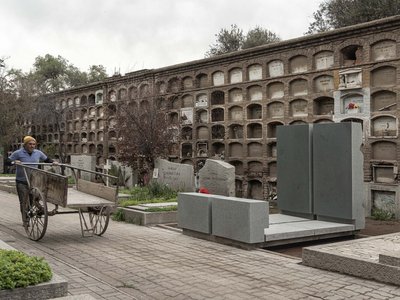 This architectural image depicts a cemetery with a man pulling a cart along a paved pathway. The cem