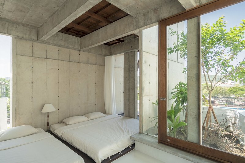 Bedroom with exposed concrete walls and ceiling opening to a planted courtyard through timber framed glazing