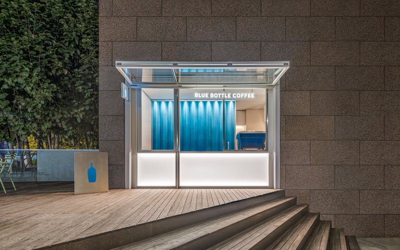 Frontal view of glass kiosk with open folding doors against brown masonry wall