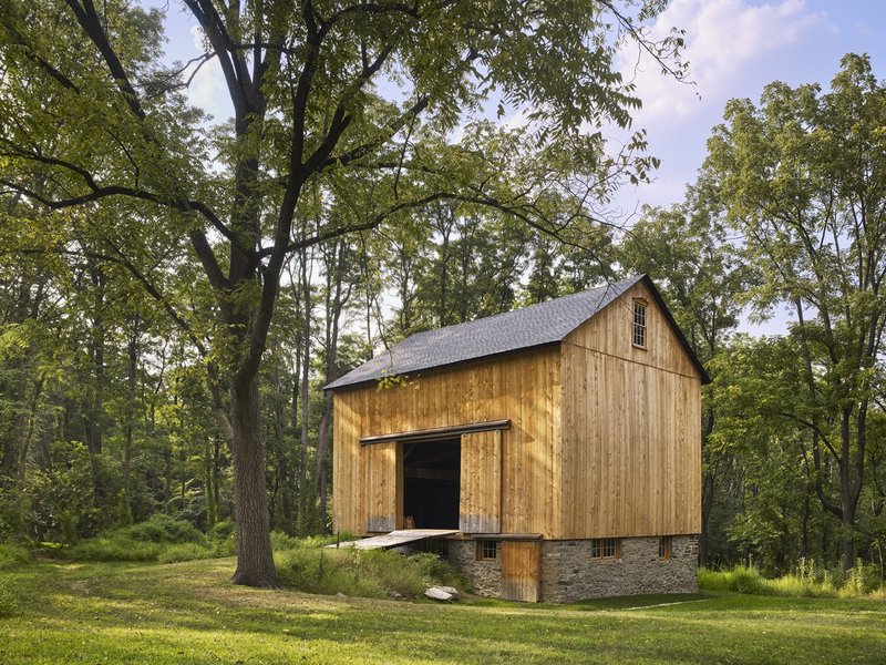 Gabled structure with vertical wood siding on a stone plinth with a person seated in the threshold