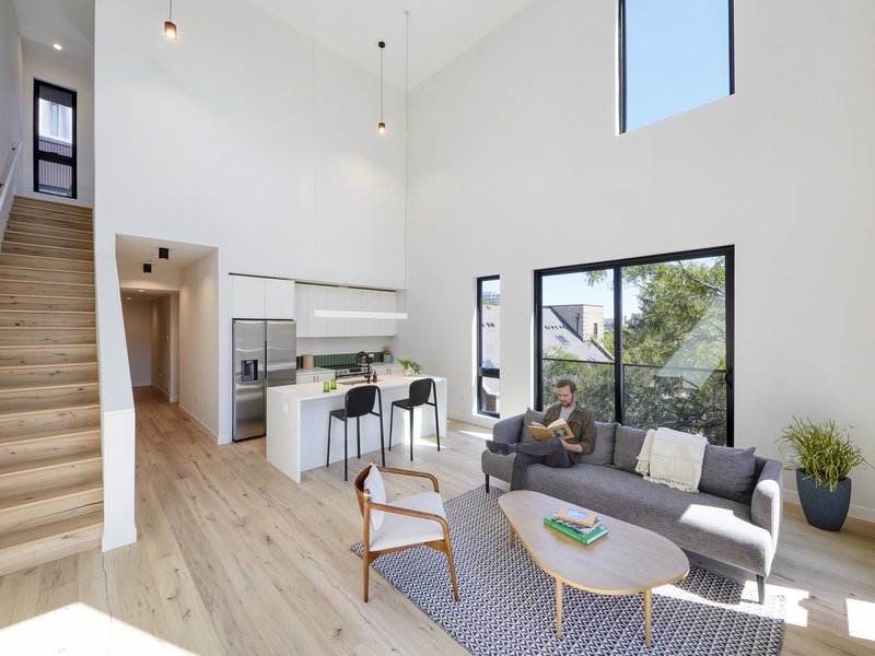 Double-height living space with white walls, timber stair, kitchen island and black-framed glazing to the street