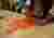 The image shows a person fixing two pieces of orange fabric together using liquid stitch. The fabric