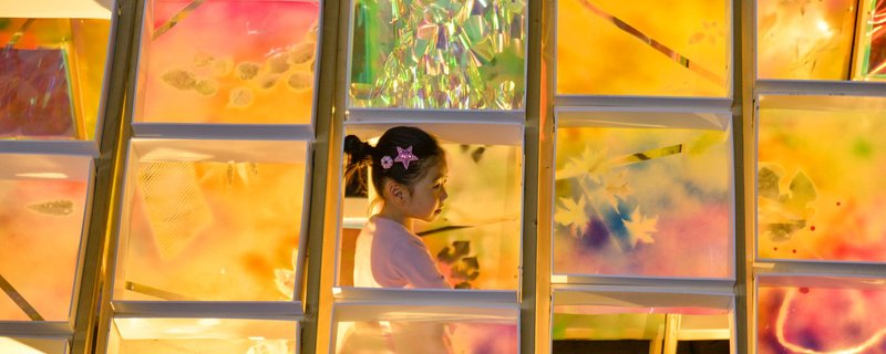 A child explores the colorful, illuminated interior of the Hi Ladders High pavilion, showcasing the beauty of creativity and architecture.