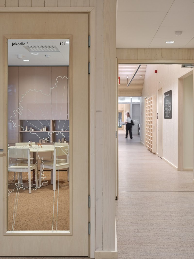 Glass door with etched tree motif and signage leading to a bright corridor