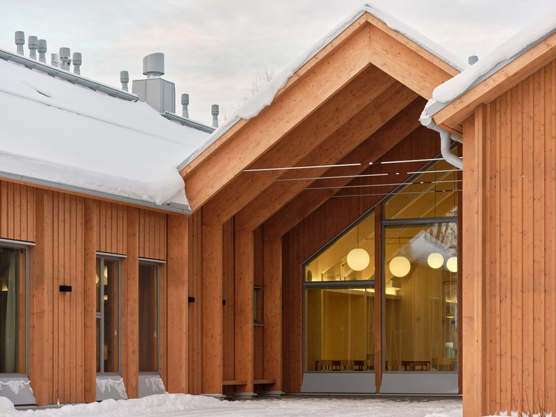 Timber gable entrance with exposed rafter structure and glazed doors under snow-covered roofs at dusk