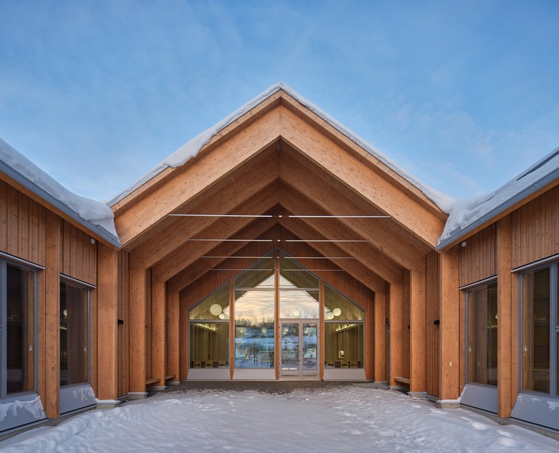 Covered courtyard entry framed by laminated timber arches leading to glazed doors in winter light