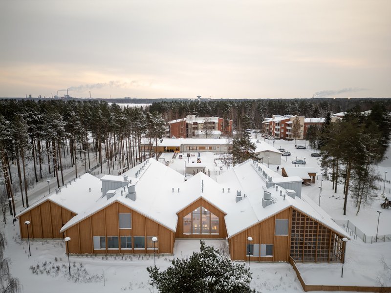 Aerial view of timber-clad gabled volumes with snow-covered roofs nestled among pine trees