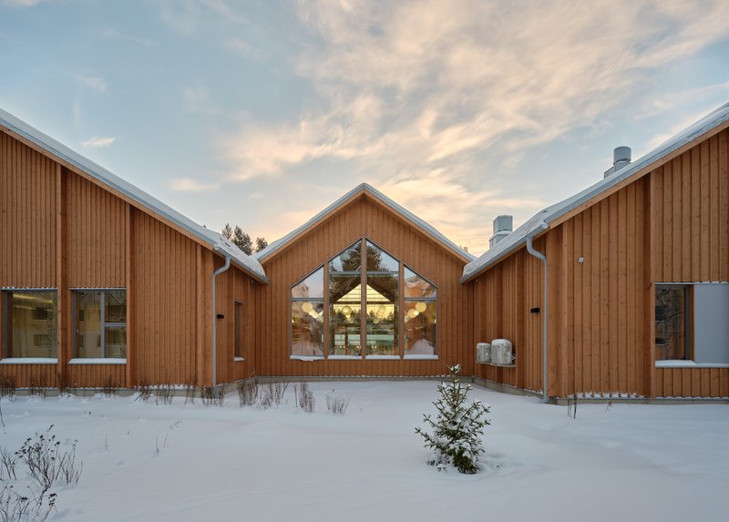 Triangular glazed gable end framed by snow-dusted timber cladding under a pastel winter sky