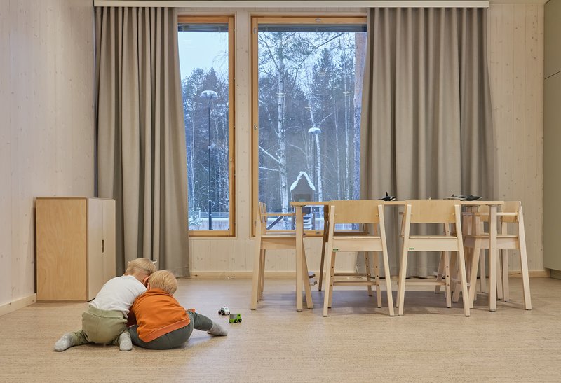 Dining area with light wood furniture and tall windows framing snow-covered birch trees at dusk