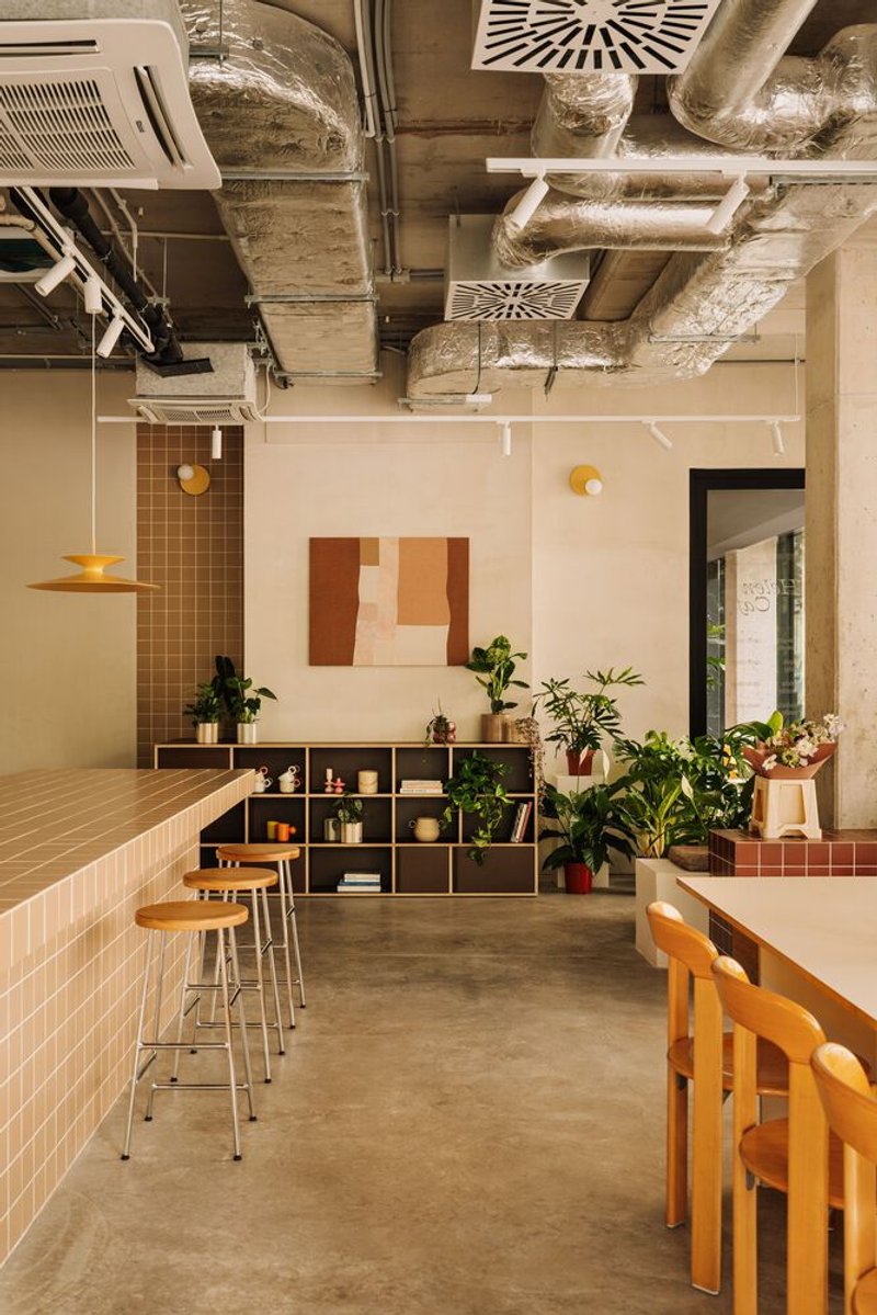 Interior showing exposed concrete ceiling with ventilation ducts above modular shelving and tiled counter with bar stools