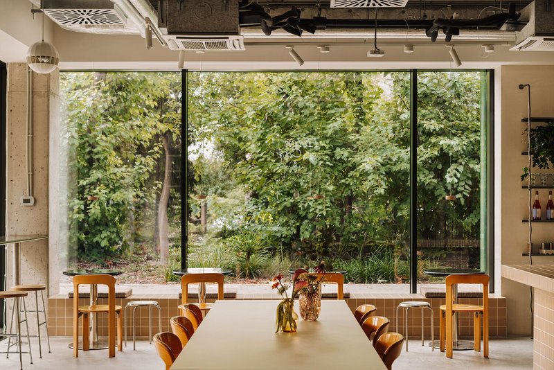 Full-height glazing overlooking a planted courtyard with timber tables and chairs arranged on polished concrete flooring
