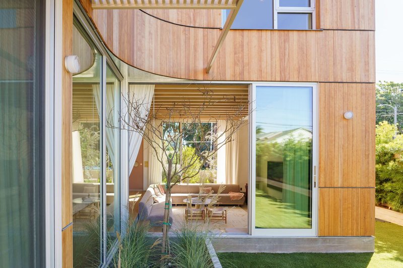 Timber-clad volume with glazed openings revealing a courtyard with a small planted tree