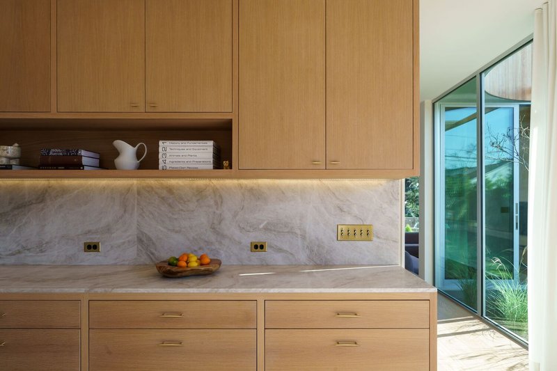 Kitchen cabinetry with marble backsplash and brass electrical outlets beside sliding glass door