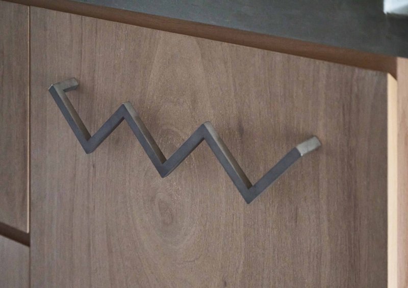 Close-up of a zigzag steel coat hook mounted on a light wood cabinet door