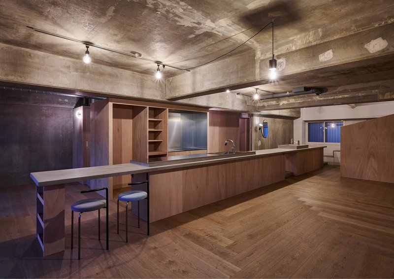Kitchen with timber cabinetry and breakfast bar beneath exposed concrete beams and track lighting at night