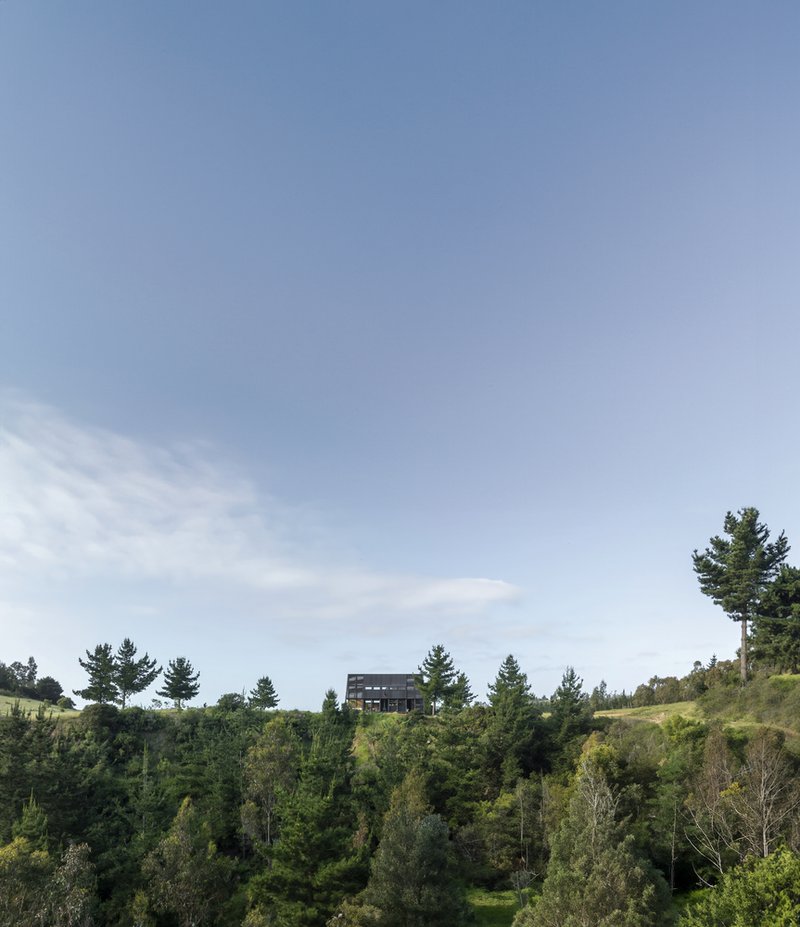 Distant view of the dark box structure perched on a hillside above dense forest vegetation