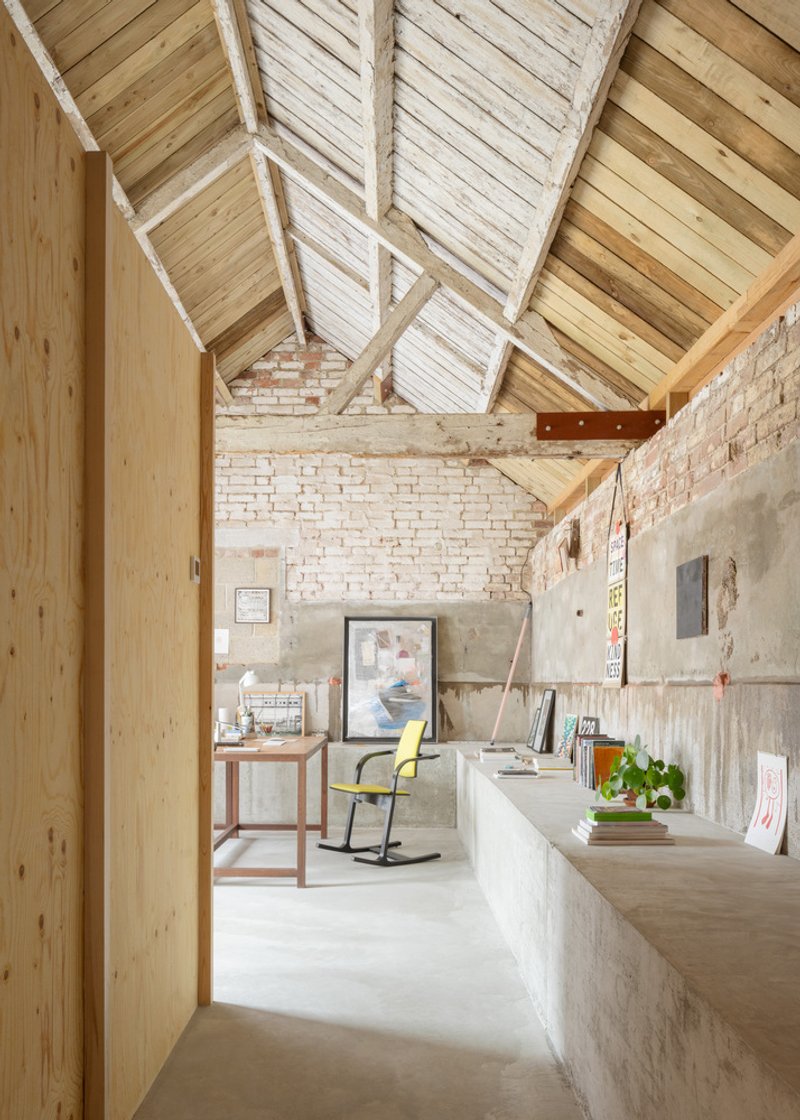 Interior workspace with exposed timber trusses, whitewashed brick walls and concrete counters beneath a vaulted ceiling