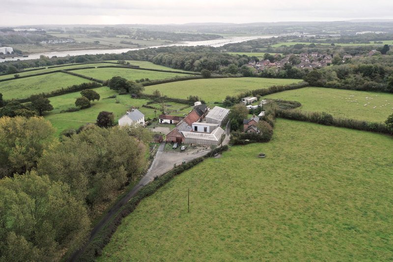 Aerial view of farm buildings clustered among hedgerows and green pastures with a river in the distance