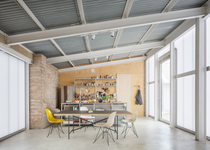 Open living space with exposed timber and corrugated ceiling beams above plywood kitchen and dining area
