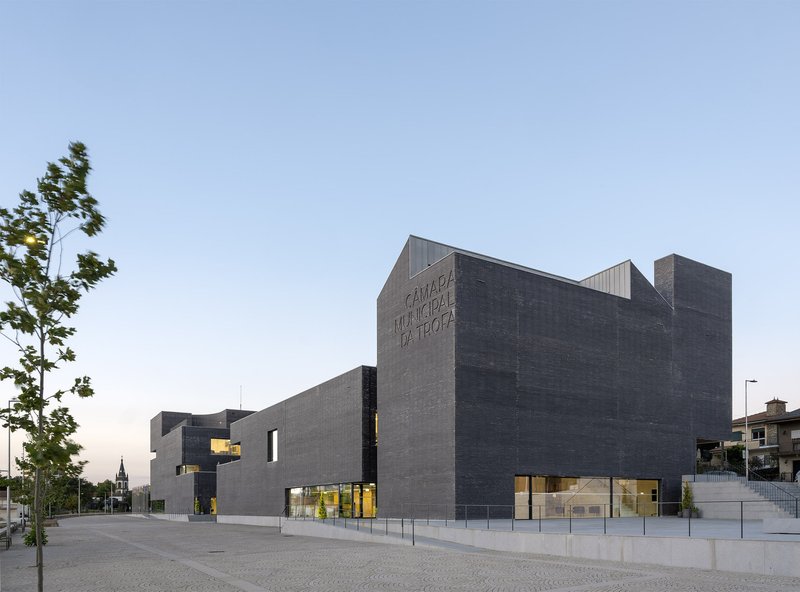 Street view of the dark brick facade with angular volumes and recessed glazing at dusk