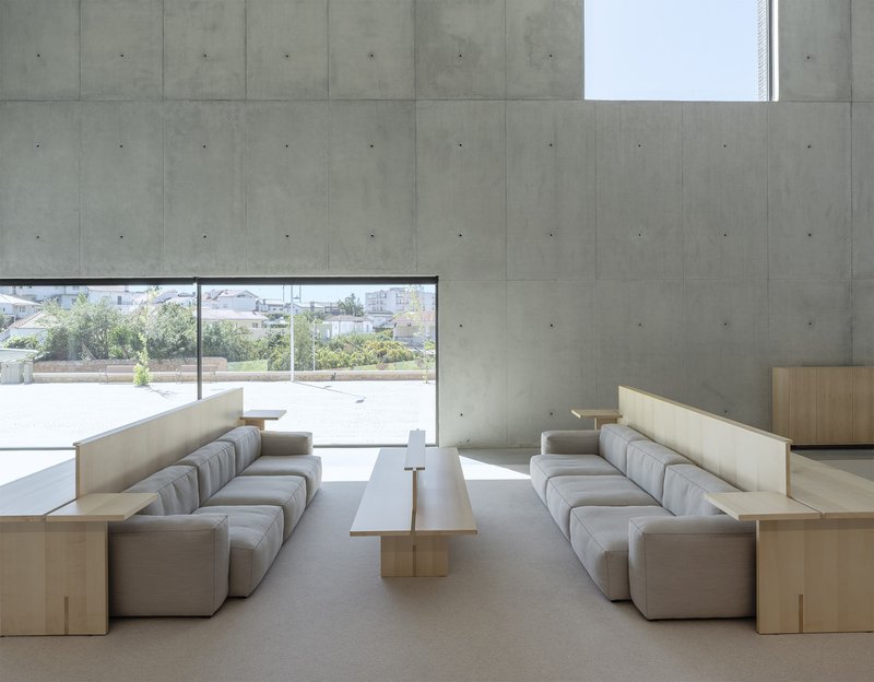 Seating area with paired modular sofas and low table facing floor-to-ceiling glazing onto exterior plaza