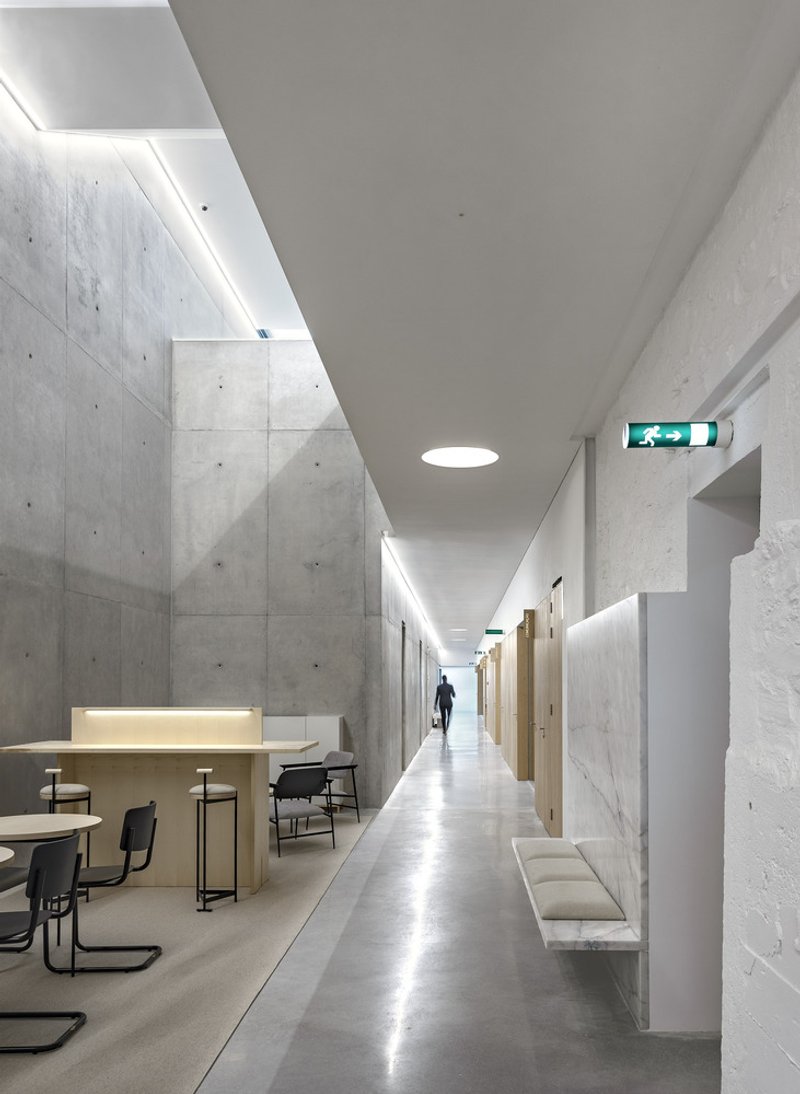 Long corridor with board-formed concrete walls, linear ceiling lights, and a figure in the distance